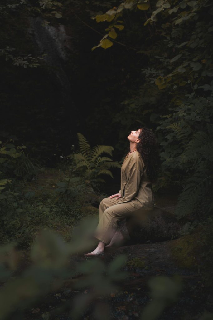 Junge Frau meditiert in einer ruhigen Waldlandschaft und genießt die Ruhe der Natur.